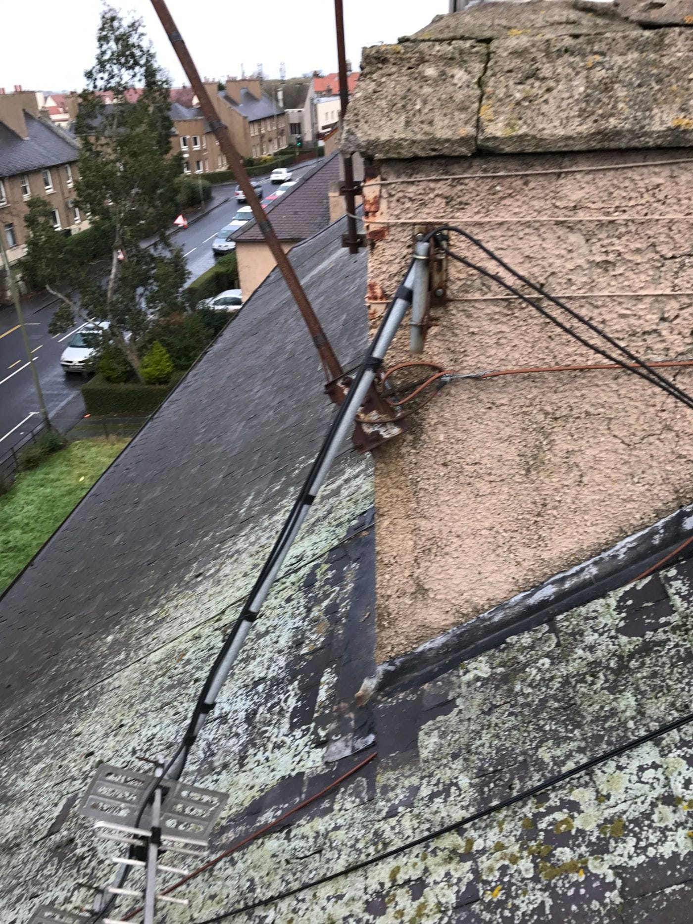 Rusted aerial brackets and loose cables on a tenement chimney